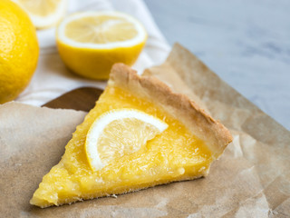 Piece of lemon tart with slice of lemons closeup on stone background, copy space.