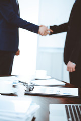 Documents and laptop on the table. Business people shaking hands on the background, silhouettes