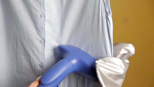 Young girl using steam system for Ironing clothes, steams blue blouse at home