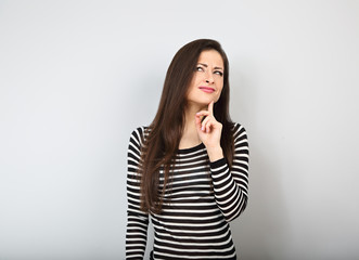Fototapeta premium Beautiful uncertain woman with finger under the face thinking and looking up in casual shirt and long hair.