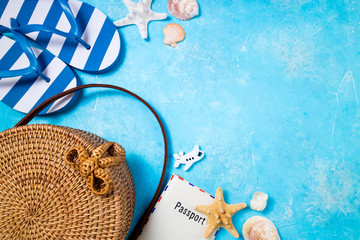 Summer female fashion beach accessories flip flop, bamboo bag and passport on blue background....