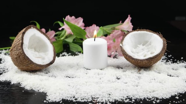 Accessories for spa treatments and aromatherapy with coconut.  Burning candle,  coconut halves,   flakes of coconut on a black background