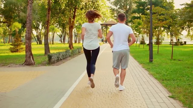 back view young couple jogging in the park. caucasian man and woman wears sportswear working out at summer morning