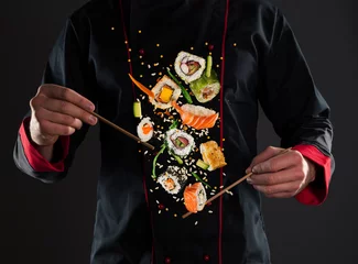 Selbstklebende Fototapeten Master chef holding chopsticks with flying sushi © Jag_cz