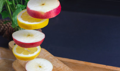 Flying (levitating) sliced apple and lemon on a rustic, dark background. Mint, blurry leaves.