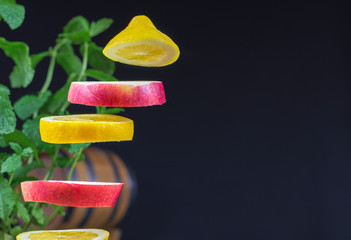 Flying (levitating) sliced apple and lemon on a rustic, dark background. Mint, blurry leaves.