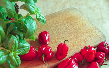 Red small paprikas on wooden cutting board. Basil leaves on the side.