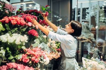 Female florist selects flowers for making bouquet - obrazy, fototapety, plakaty