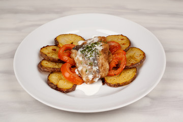 Baked potatoes in the peel sliced with tomato and grilled meat in a white sauce.