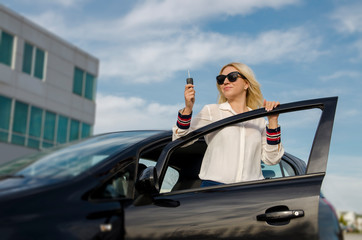 Naklejka premium Beautiful woman in her car standing with open doors and holding key