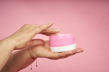 Senior woman hands applying cream on hands on coral background