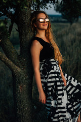 Young beautiful woman wearing fashionable dress and mirrored sunglasses walking in a rural area