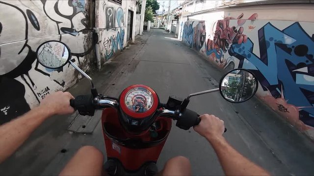 POV shot of a man driving a moped through a backalley street in Chiang Mai, Thailand.