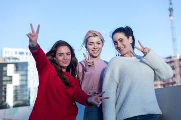 Front view of three Teenage girls making a peace sign outdoors in a sunny day