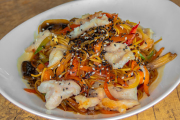 Nuddles with chicken. Rice nuts with carrots, zucchini, mushrooms, peppers, chicken pieces, teriyaki sauce, white and black sesame. Closeup.