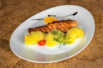 Grilled salmon fillet with mashed potatoes. And stalk dill, cherry tomato, a piece of lemon and pomegranate sauce. In a white plate on a wooden background.