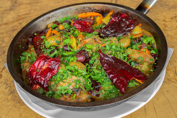 Vegetables roasted on a pan. Dried red peppers, eggplant, carrots, onions, garlic, potatoes, black and green olives and spices. Sprinkle with fresh parsley. On a wooden background.