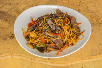 Noodles with veal and vegetables. Mushrooms, zucchini, peppers, carrots in a sweet-sour sauce. Sprinkled with white and sesame seeds. Isolated on white background.