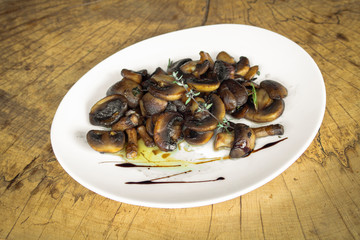 Mushrooms roasted with butter. With thyme and rosemary. In a white plate on a wooden background.