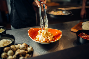 Chef with pan cooking pasta on wooden table