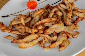 Crispy fried pork slices. Garnished with cherry tomatoes and balsamic sauce. Closeup.
