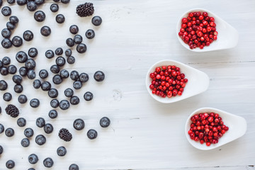 Berries platter with fresh organic red cowberry, blueberry and blackberry wooden table, top view.