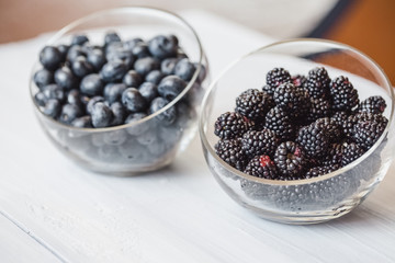 Plates with blueberry and blackberry closeup on a wooden table.