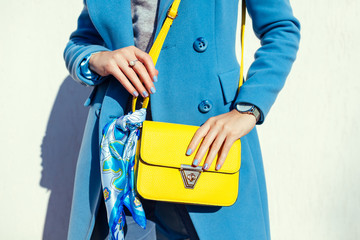 Young woman holding stylish handbag and wearing trendy blue coat. Spring female clothes and accessories. Fashion