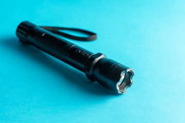 A black metal flashlight with shocker at the blue background. protection and security concept. for design and decoration