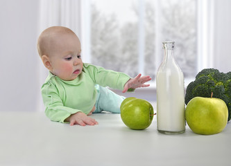 Fototapeta premium Small child reaches for a fresh green apple on a white table