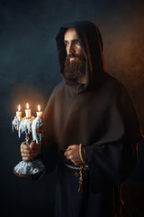 Medieval monk in robe holds a candlestick in hands