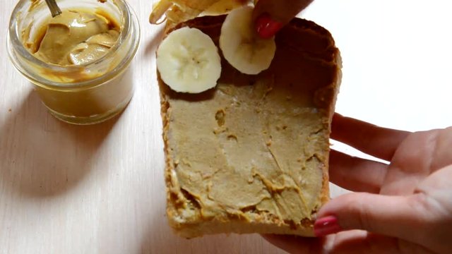 girl woman makes Homemade peanut butter and bananas for healthy breakfast or picnic. Homemade peanut butter ingredients: peanuts (roasted, unsalted, shelled), peanut oil, honey. No salt, no sugar.