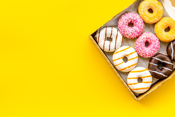 Donuts with different flavors in box on yellow background top view mockup