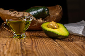 Half avocado fruit and avocado oil in a glass bowl on old rustic table. Healthy eating, diet, body care and hair care concept.