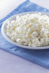 Cottage cheese on blue napkin. Cheese on white plate with wooden spoon. Soft cheese for diet. Healthy dairy product for breakfast