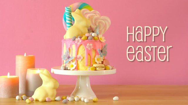 On trend Easter candy land drip cake decorated with lollipops, cand eggs and white chocolate bunny in party table setting, with animated text greeting.