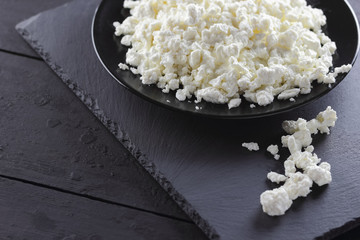 Cottage cheese on black slate board. Cheese on black plate. Soft cheese for diet on black boards. Healthy dairy product for breakfast. Concept