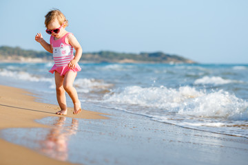 Fototapeta na wymiar Cute curly baby girl playing on a beautiful tropical beach wearing a cute swimsuit