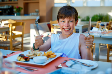 Happy cute boy is starting his dinner. Holding a spoon and fork in the hand