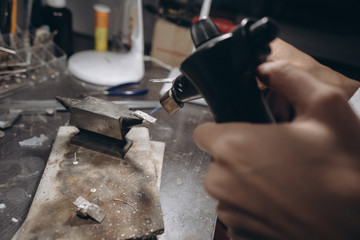 In the workshop, a woman jeweler is busy soldering jewelry