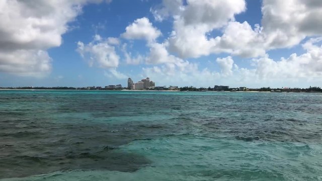 Motion time lapse of white fluffy clouds, boats and a parasailing passing by in the Bahamas