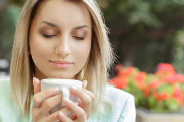 Coffee aromatherapy. Close up portrait of a relaxed beautiful young female holding a cup of coffee sitting on the terrace