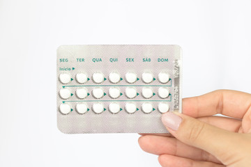 Woman hand holding oral contraceptive pill with white pills white background. Days of the week in Portuguese. Brazil.