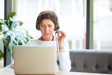 Aged stylish woman speaking via laptop in cafe