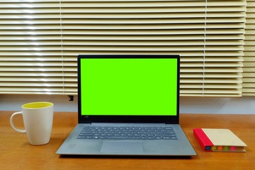 laptop and cup of coffee on wooden table with green chroma key