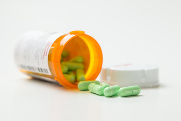 Prescription medicine green capsules cascading out of orange pharmacy bottle