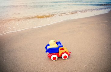 Yellow duck toy and colorful car on sand in the beach