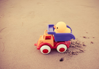 Yellow duck toy and colorful car on sand in the beach