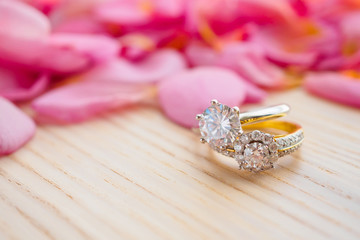 Jewelry diamond wedding ring on wood table with beautiful pink rose petal background close up