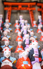 Close up of colourful fox statues (Kitsune) lined up in front of a small torii gate at the Fushimi Inari Taisha Shrine in Kyoto, Japan